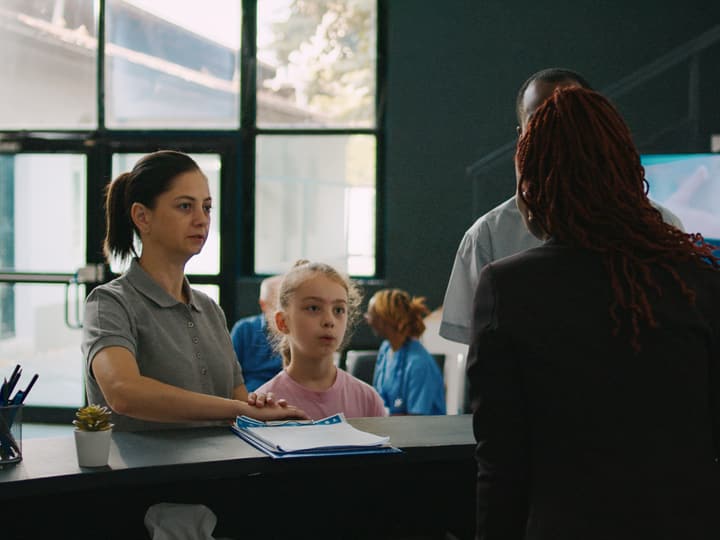 A receptionist welcoming a family at a clinic front desk