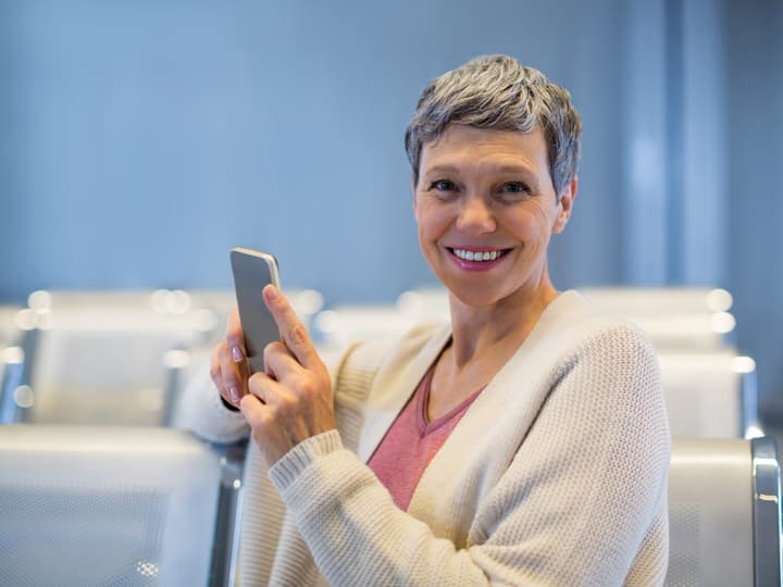 A smiling woman checking her phone in a clinic waiting area