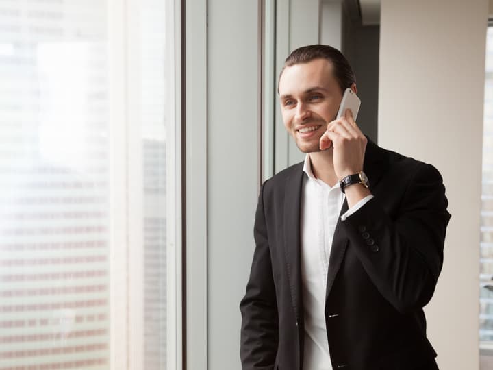 A smiling man on a phone call by an office window