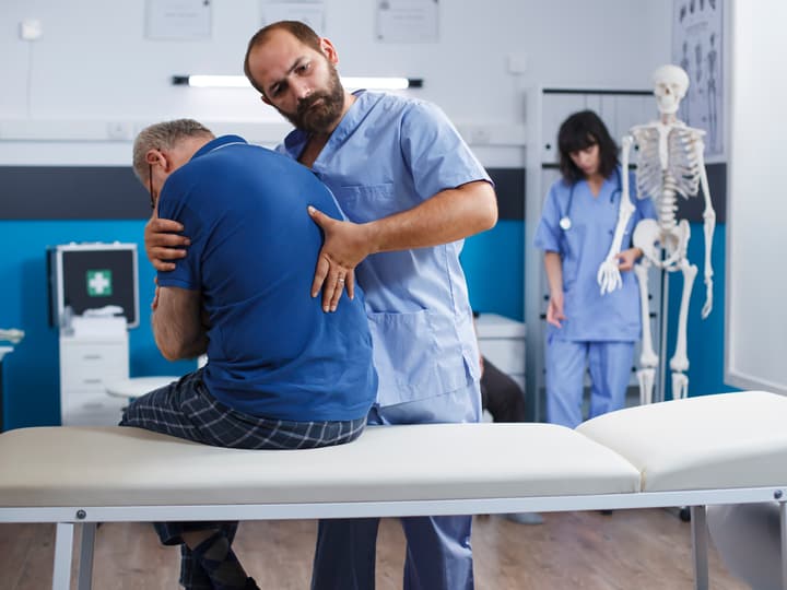 A chiropractor assessing a seated patient’s back in a treatment room