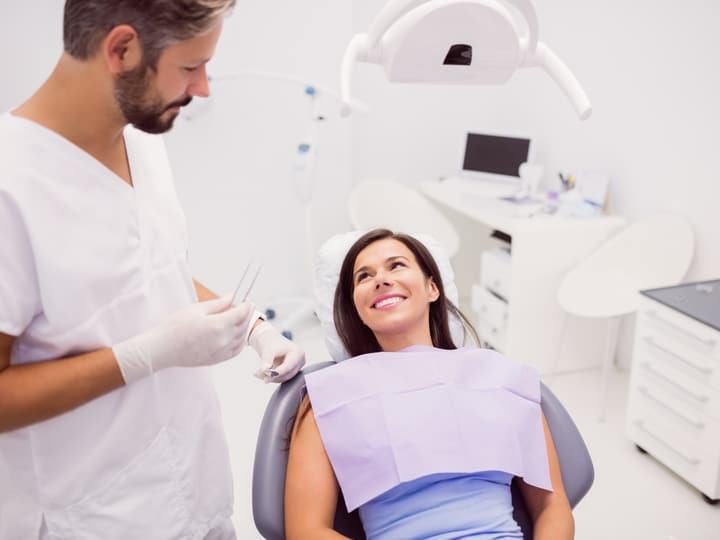 A dentist in gloves talking with a smiling patient in the dental chair