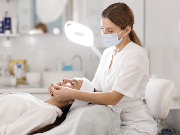 A practitioner giving a client a facial treatment in a bright clinic room