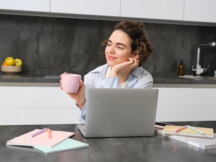 A woman with a coffee browsing a website on her laptop at home